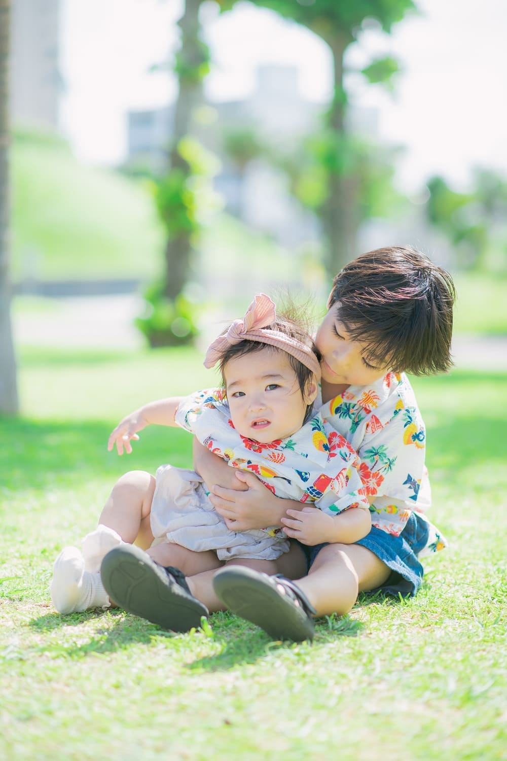 芝生の上で妹を抱きしめるかりゆし姿のお兄ちゃんの様子