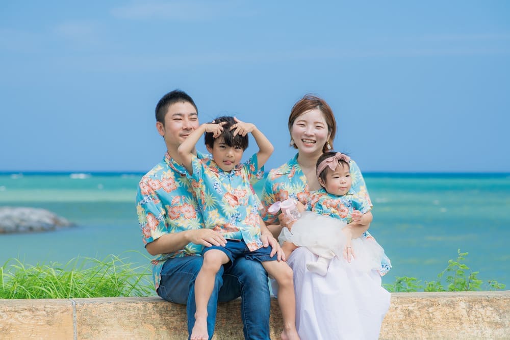 沖縄の海を背景にかりゆしウェアで並んで座る家族4人の姿