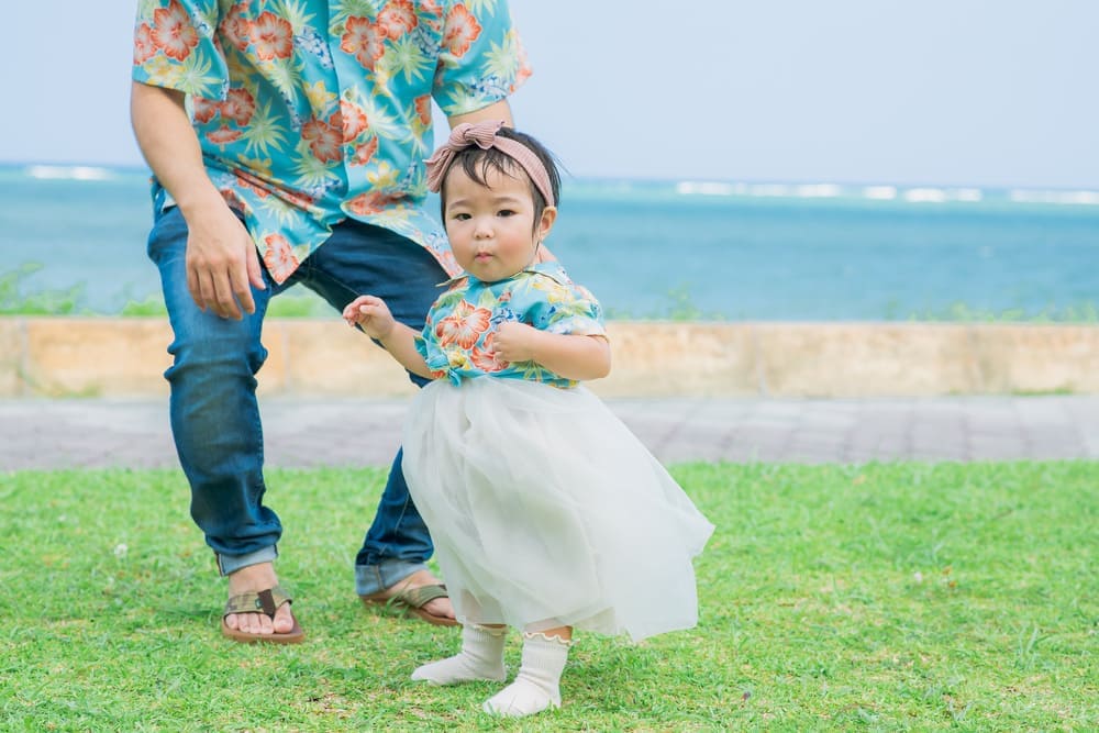 かりゆしウェアをおそろいで着た家族が海辺に並んで立っている様子