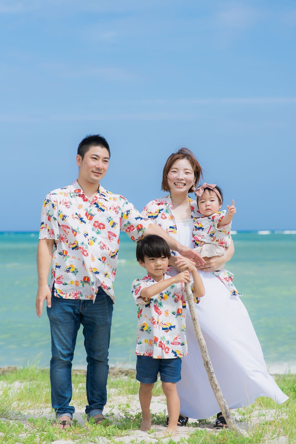 沖縄の海をバックにかりゆしウェアで微笑む家族4人のアップ写真