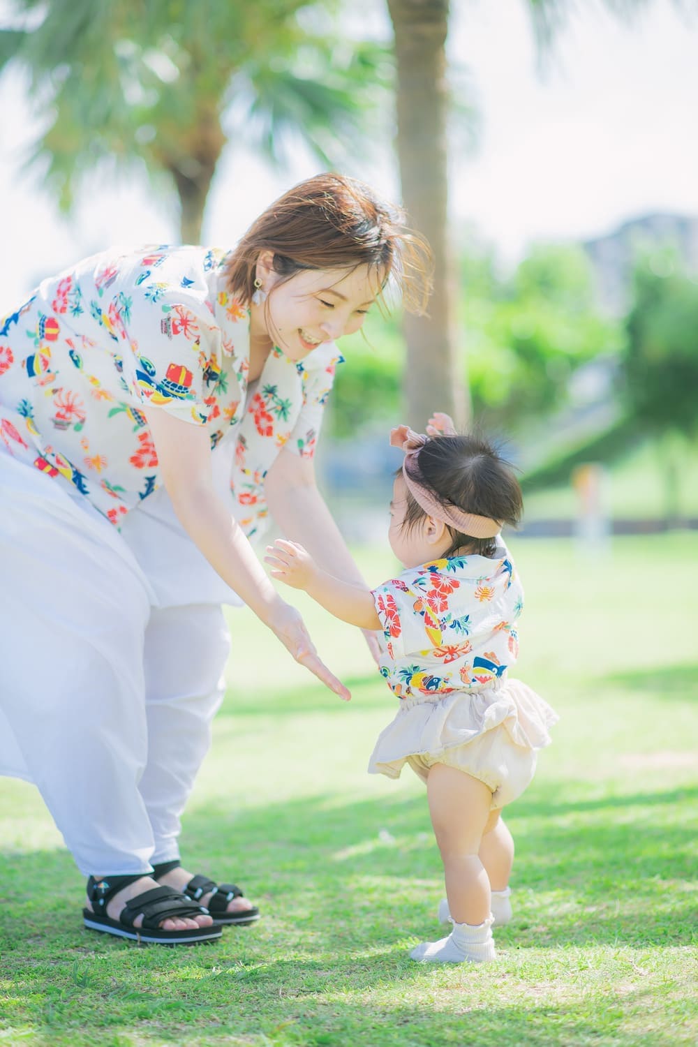 芝生の上でママに向かってよちよち歩くベビーの姿