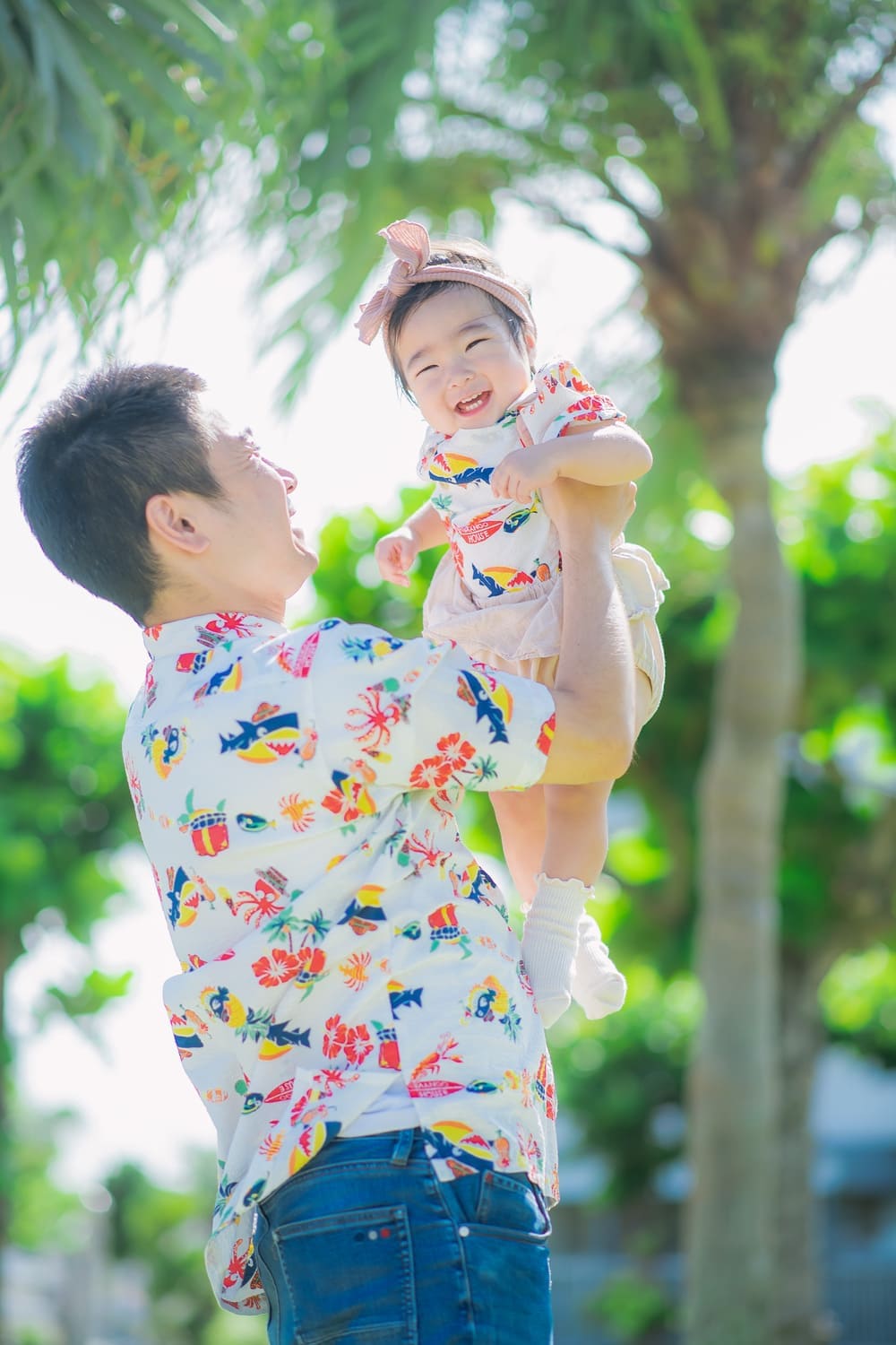 パパに高く抱き上げられて笑顔を見せるベビー