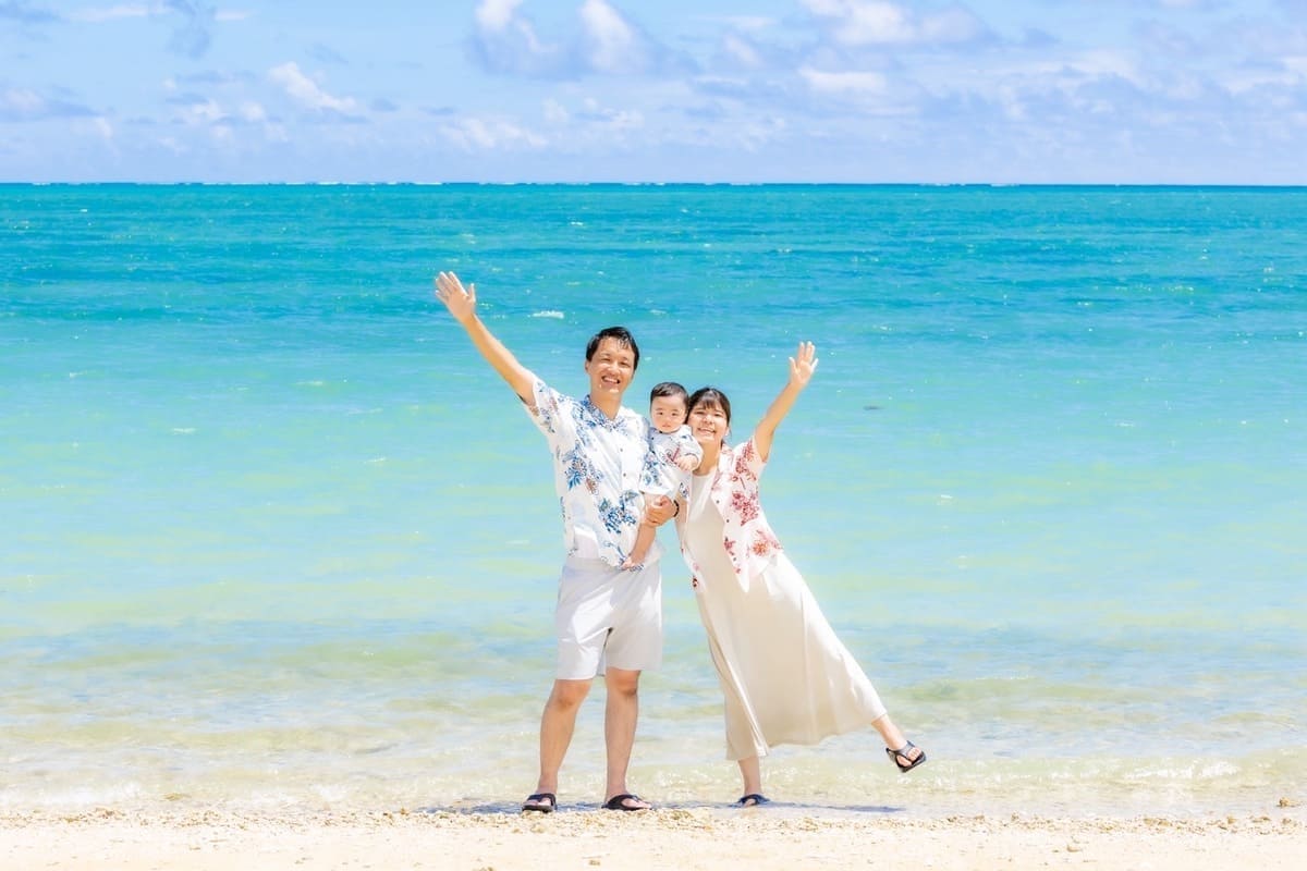 沖縄の海に向かって家族3人で手をあげている様子