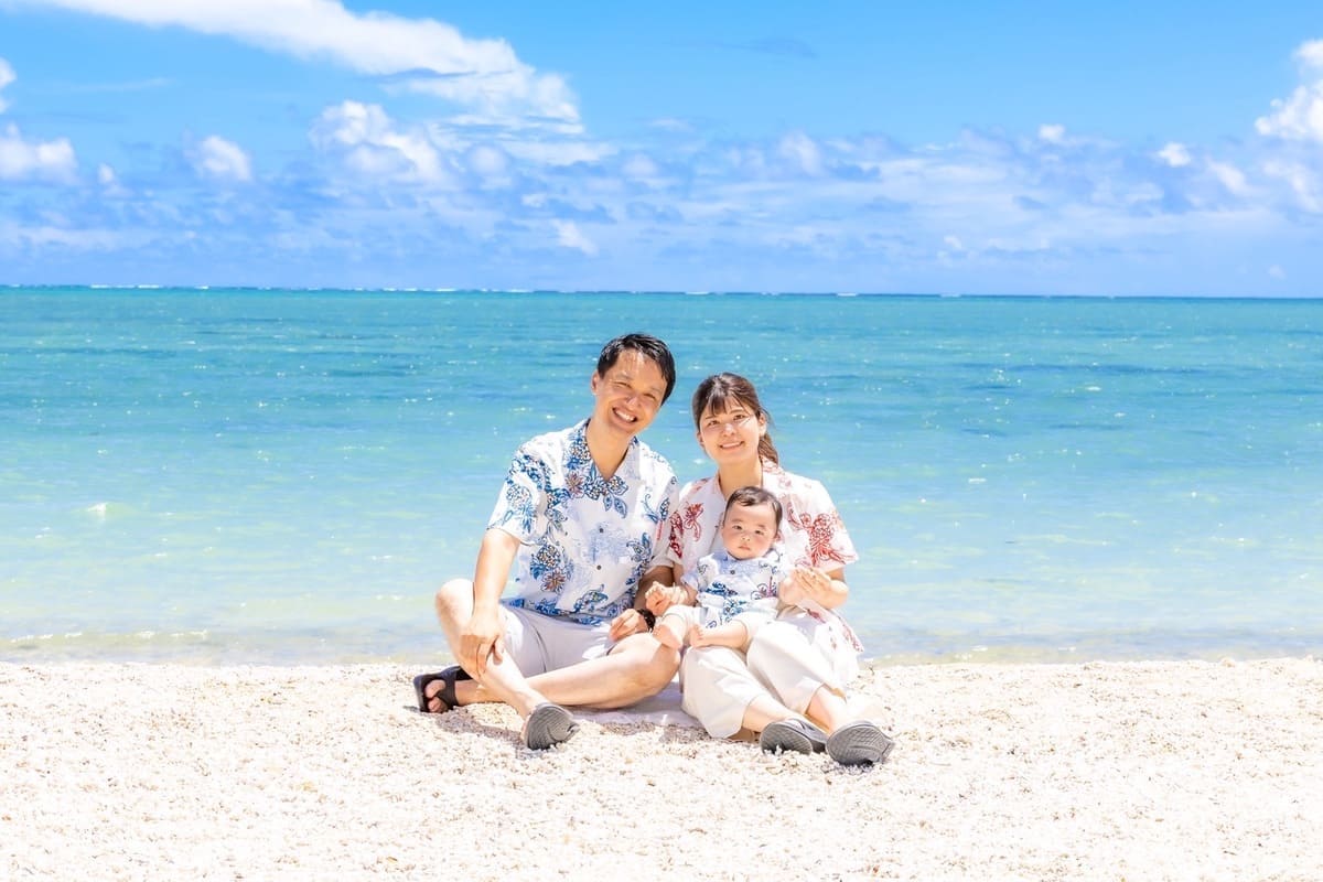 砂浜に座りかりゆしウェアを着てこちらを見る赤ちゃん