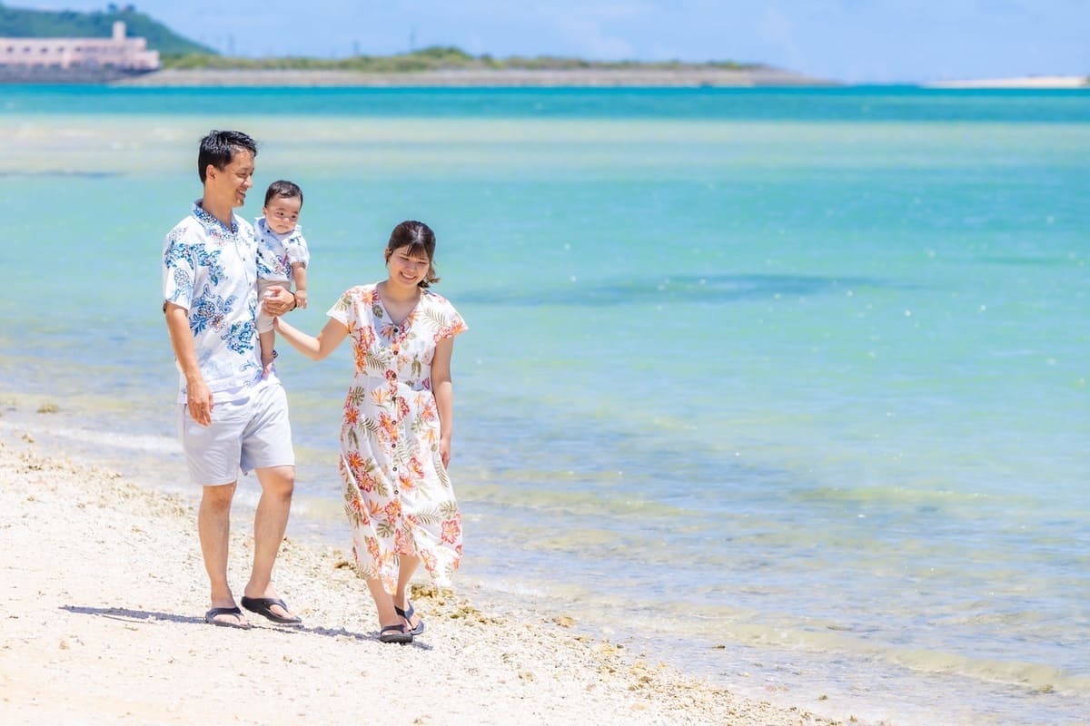 沖縄の海を背景にかりゆしウェアで微笑む家族のアップ写真