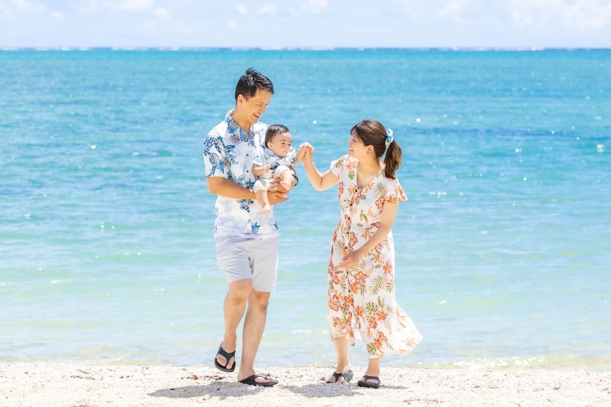 かりゆしウェアを着た家族が沖縄のビーチを手をつないで歩く様子