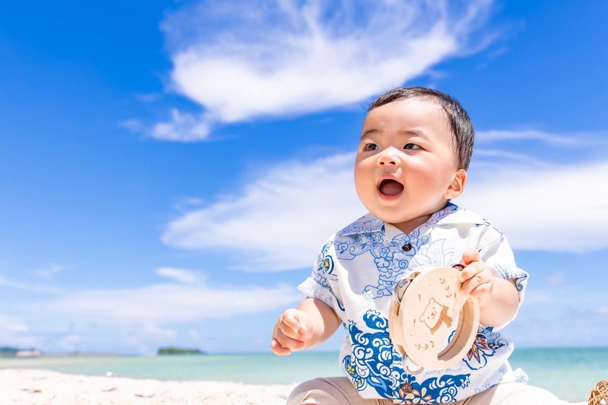 ビーチで記念プレートを持ち笑顔を見せる赤ちゃん