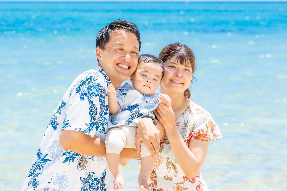 沖縄のビーチでかりゆしウェアを着た家族が並んで座っている様子