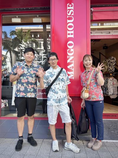 マンゴハウス国際通り2号店の入口看板前で記念撮影するお客様3人